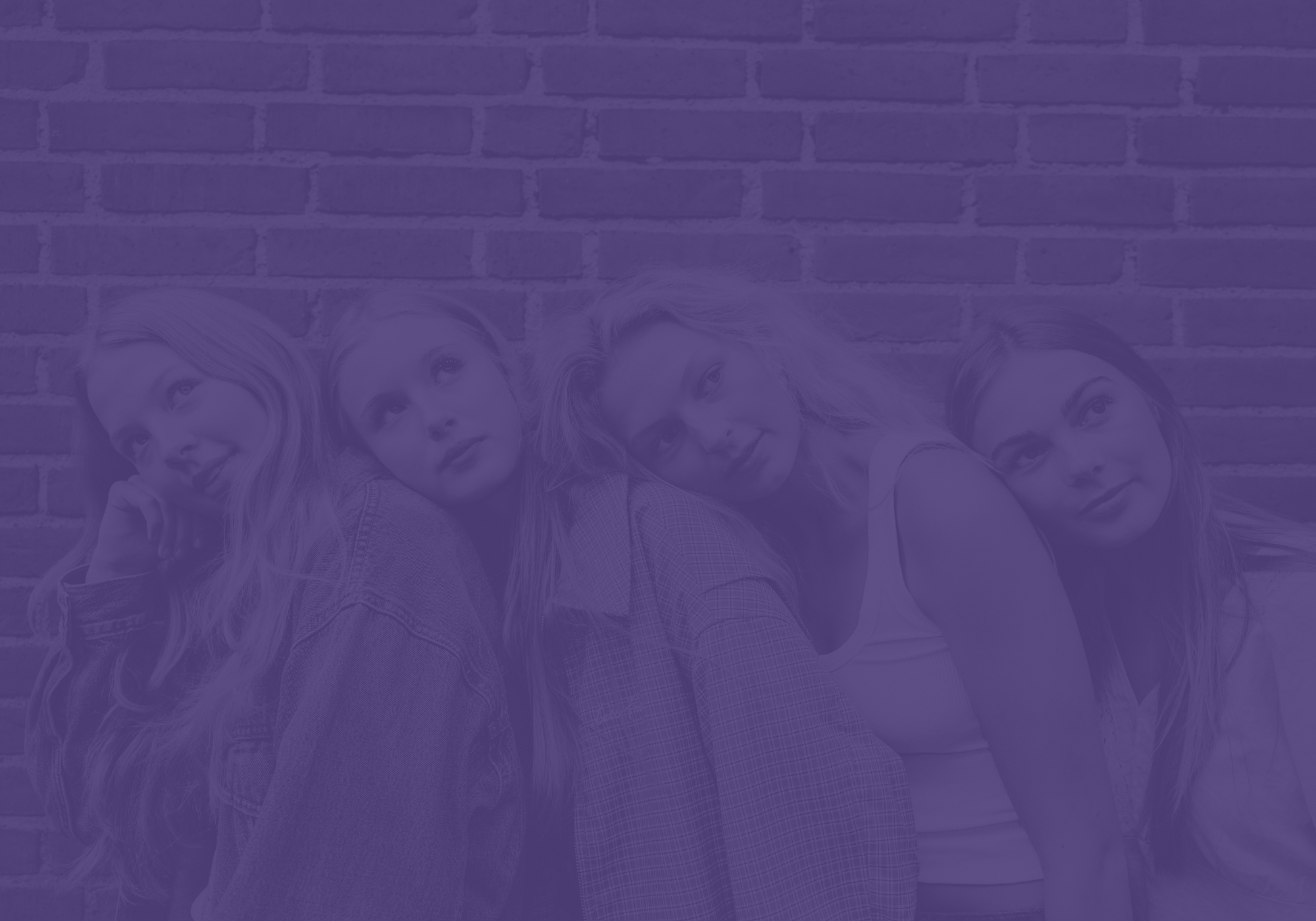 Four women leaning together in front of a brick wall with purple overlay.